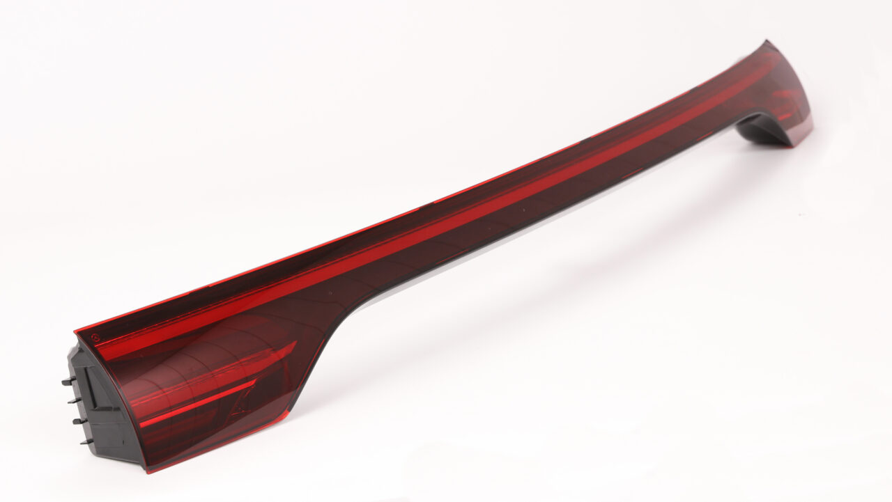 Elongated automotive rear light module with red transparent cover and black housing, manufactured using laser plastic welding.